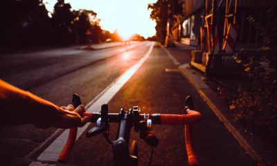 Es ist im Vordergrund ein Fahrradlenker zu sehen, im hintergrund eine Straße und der Sonnenuntrgang.