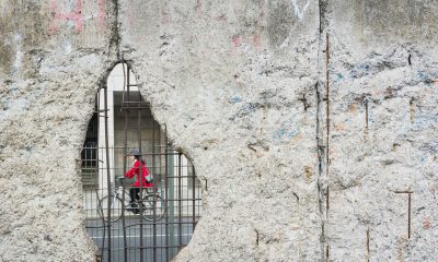 Es ist eine Radfahhrerin durch ein Loch in der Berliner Mauer zu sehen