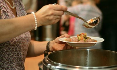 Frau schöpft Suppe aus einem großen Topf in einen Teller
