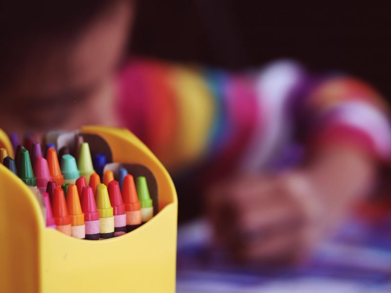Bunte Stifte mit malendem Kind im Hintergrund