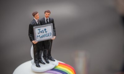 Auf dem Bild ist die Verzierung einer Torte zu sehen. Zwei Männer aus Zuckerguss halten ein Schild mit der Aufschrift "Just married".