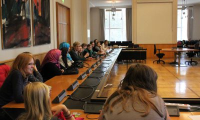 Das Bild zeigt Mädchen, die in einem Sitzungssaal im Kreis sitzen und einige grüne Abgeordnete.