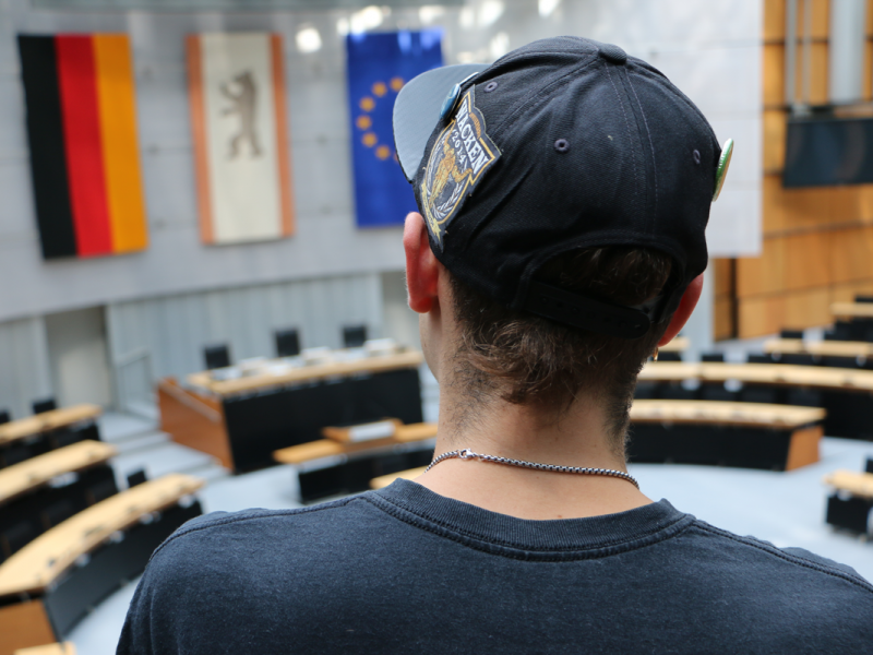 Auf dem Bild ist ein junger Mann von hinten zu sehen, der auf der Besuchertribüne des Plenarsaals im Berliner Abgeordnetenhaus steht.