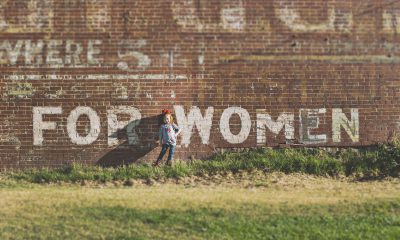 Es ist ein junges Mädchen zu sehen, das vor einer Wand steht, auf der "For Woman" steht
