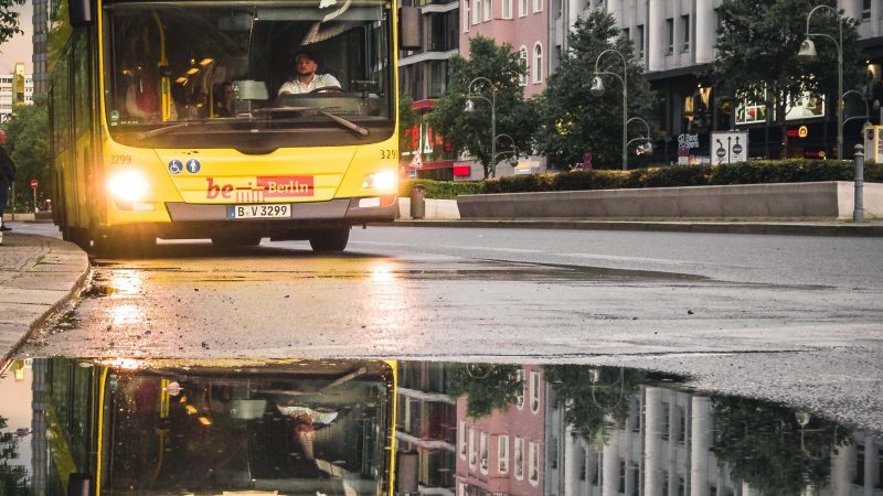 Ein Bus fährt auf der Straße und spiegelt sich in einer Pfütze