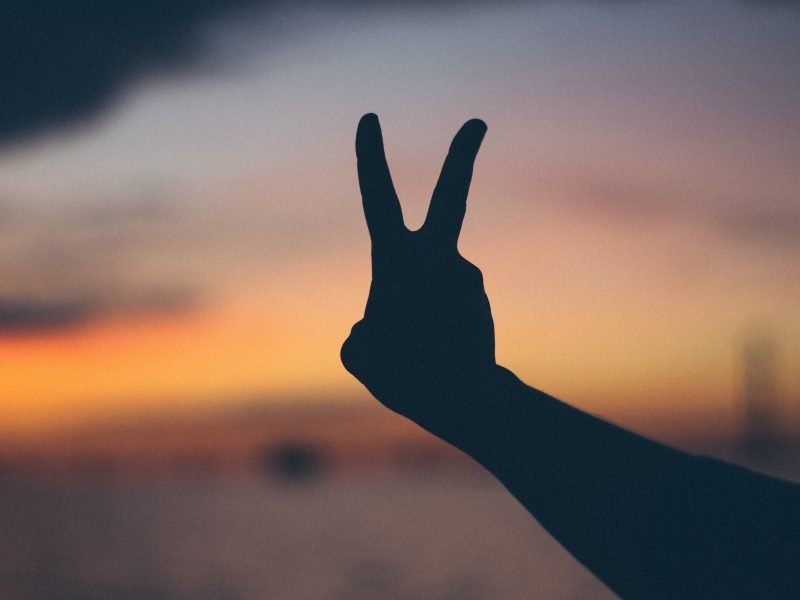 Es ist eine ausgestreckte Hand, die das Friedens-zeichen hochhält, vor dem Sonnenuntergang zu sehen