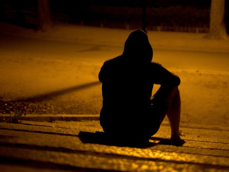 ein Mensch sitzt nachts, allein auf der Straße