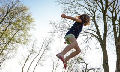 Kind springt auf einem Trampolin in die Höhe; das Foto ist so gemacht worden, dass nur ein Kind und Bäume, die in den Himmel ragen, zu sehen sind.