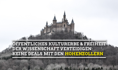 Bild mit geringer Sättigung auf welchem die Burg Hohenzollern, die auf einem Berg mit Bäumen steht, abgebildet ist. In der Bildmitte steht in weißer Schrift: Öffentliches Kulturerbe und Freiheit der Wissenschaft verteidigen: Keine Deals mit den Hohenzollern, wobei das letzte Wort gelb ist.