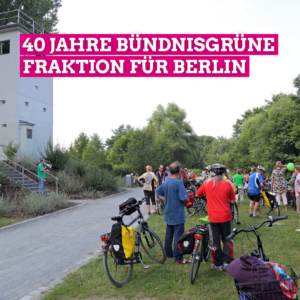 Michael Cramer steht mit einem Megafon neben einem Stasi-Überwachungsturm auf dem Mauerradweg und spricht zu einer Menschengruppe mit Fahrrädern, die gemeinsam mit ihm den Mauerradweg fahren.An der Bildoberseite steht in großen weißen Buchstaben, die pink unterlegt sind, 40 Jahre Bündnisgrüne Fraktion für Berlin.