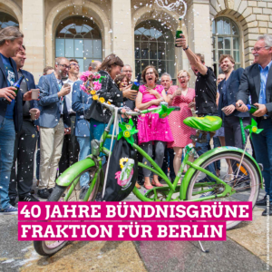 Das Bild zeigt die Bündnisgrüne Fraktion beim Feiern über das verabschiedete Mobilitätsgesetz. In der Bildmitte steht ein Grünes Fahrrad, weches mit Papierwindrädern und Blumen geschmückt ist. Die Grüne Fraktion steht im Halbkreis um dieses Fahrrad herum und Georg Kössler erzeugt durch die Flasche in seiner Hand, die er hoch in die Luft hält, einen Sektregen, der Fahrrad und Fraktion erreicht. Auf dem Bild steht außerdem in großer weißer Schrift, die pink unterlegt ist, 40 Jahre Bündnisgrüne Fraktion für Berlin.