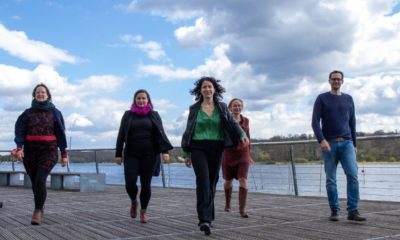 Silke Gebel, Antje Kapek, Bettina Jarasch, Petra Budke und Benjamin Raschke, letztere sind die Vorsitzenden der Grünen Fraktion im Brandenburger Landtag, laufen auf die Kamera zu. Im Hintergrund ist ein Gewässer und ein Ufer mit Bäumen zu sehen, während die 5 Person auf einer Holzplattform laufen.