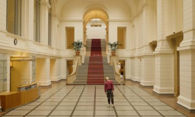 Auf dem Bild ist die Eingangshalle des Abgeordnetenhauses zu sehen in deren Mitte eine Person mit brauner Hose und rotem Pulli steht, die in die Höhe schaut.