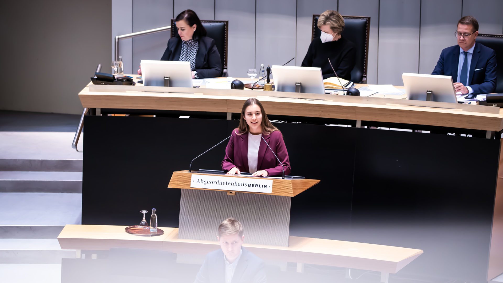 Klara Schedlich am Redepult des Abgeordnetenhauses. Sie hält eine Rede und trägt einen weinroten Blazer.