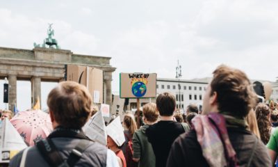 Demonstration vor dem Brandenburger Tor, Menschenmenge von hinten. Man sieht ein Plakat, auf dem steht "Wake up" mit einer brennenden Weltkugel