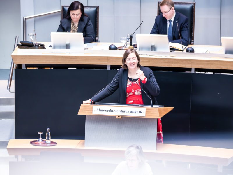 Silke Gebel steht am Rednerpult des Abgeordnetenhauses. Sie trägt ein rotes Kleid und gestikuliert beim Sprechen mit ihrer linken Hand.