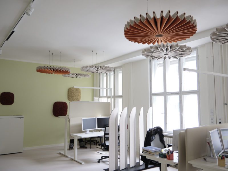 Zu sehen ist ein modernes Büro in einem hellen Raum. Auf einem Schreibtsich stehen zwei Bildschirme, an der Decke hängt eine stilvolle Lampe.