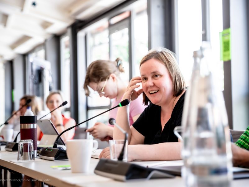 Cathrin Wahlen, eine Frau mit einem Bob-Haarschnitt, sitzt an einem Tisch und spricht in ein Mikrofon.