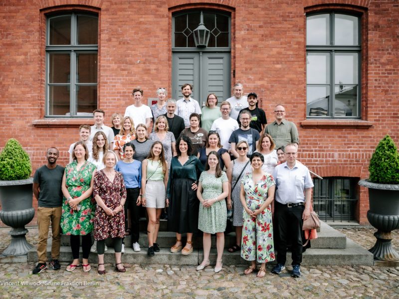 Ein Gruppenfoto aller Beteiligter der Fraktionsklausur 2023. Es stehen ca. 35 Personen hintereinander auf einer Treppe vor einem Backsteingebäude. Sie sind sommerlich gekleidet und lächeln alle.