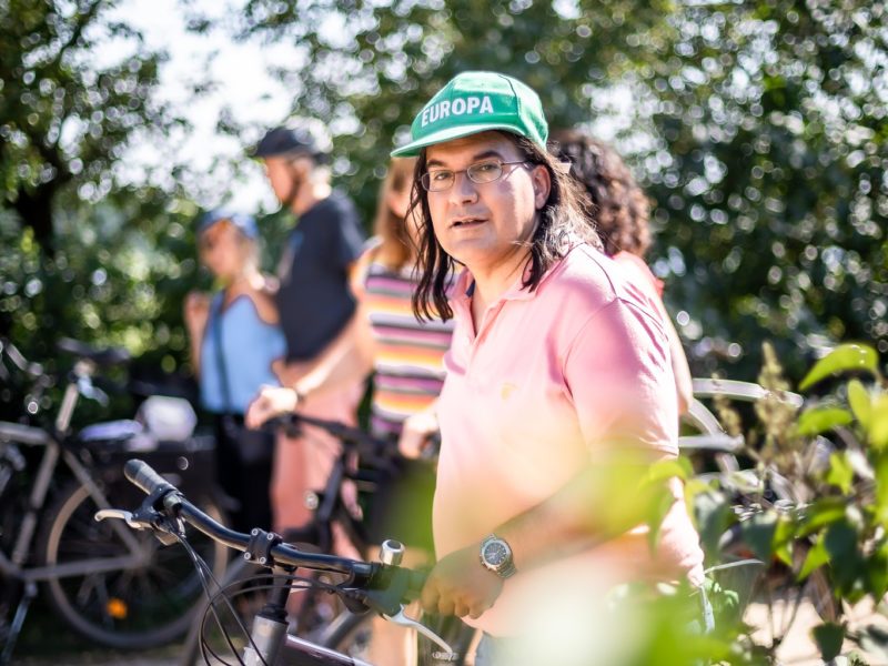 Alexander Kaas-Elias steht mit seinem Fahrrad im Grünen, im Vordergrund Blätter.