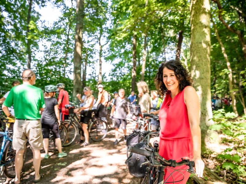 Eine Gruppe von Radfahrern im Wald, vorn im Bild Bettina Jarasch, die in die Kamera lächelt.