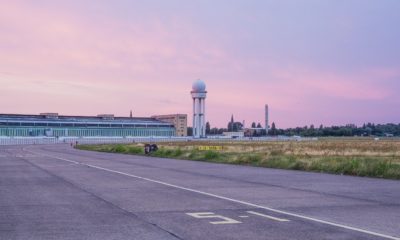 Das Tempelhofer Feld in der Dämmerung, der Himmel ist in rosa und lila eingefärbt. Im Hintergrund das alte Flughafengebäude und der Radarturm.