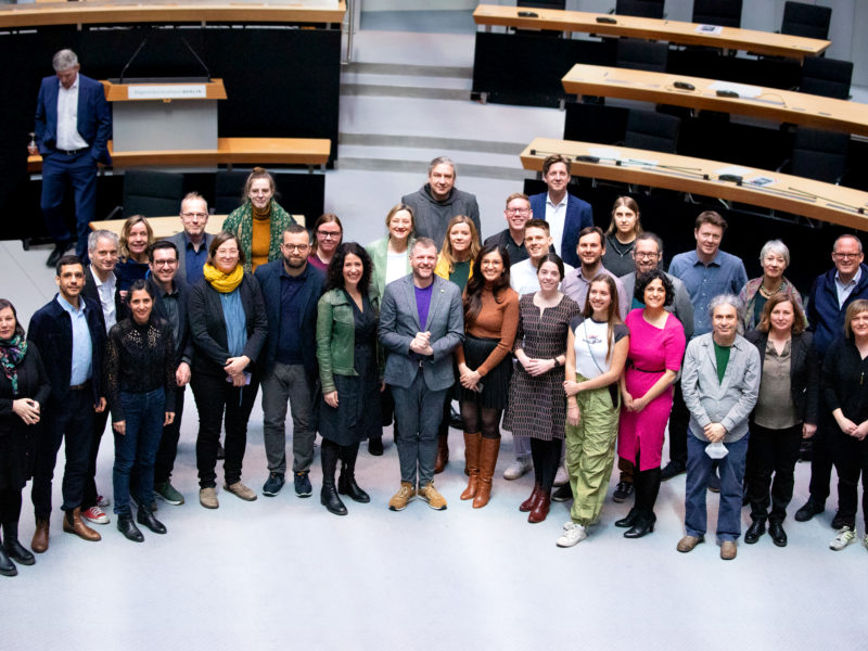 Auf dem Foto sind die Abgeordneten der Fraktion Bündnis/90 Die Grünen im Abgeordnetenhaus von Berlin zu sehen. Sie stehen im Plenarsaal und blicken nach oben in die Kamera