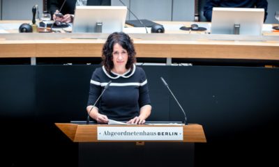 Foto von Bettina Jarasch bei ihrer Rede im Abgeordnetenhaus. Sie steht am Redepult und schaut durchdringend. Sie hat mittellange schwarze Locken und trägt ein schwarzes Kleid mit weißem Kragen.
