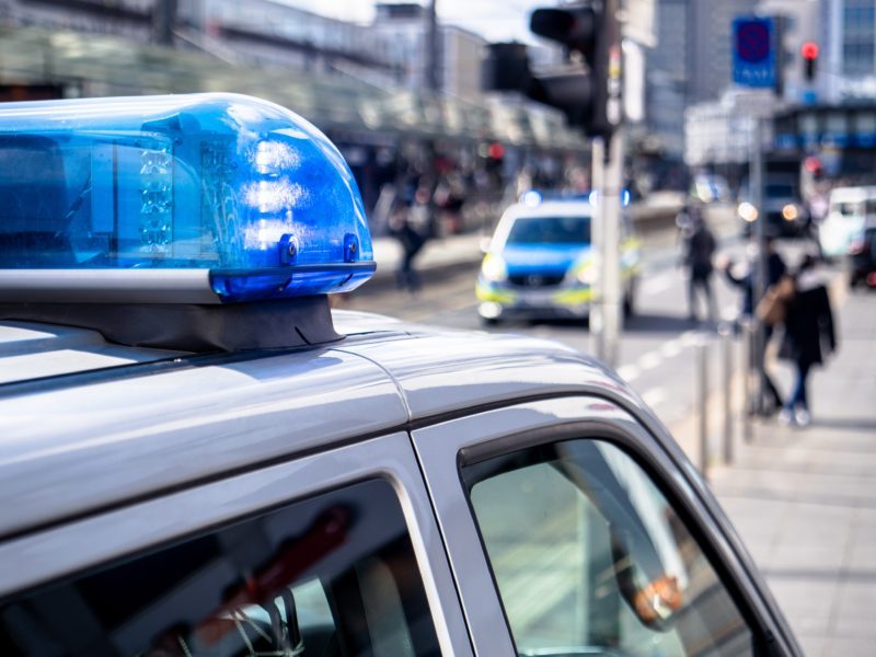 Auf dem Bild ist das Dach eines Polizeiautos zu sehen mit Blaulicht, im Hintergrund weitere Polizeiautos.