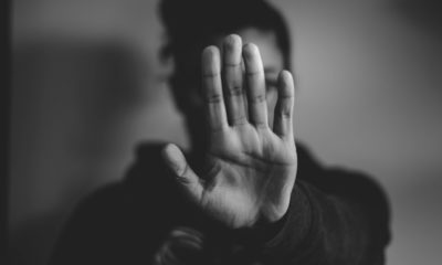 Schwarz-weiß Foto von einer Frau, die ihre Hand zum Schutz vor sich ausstreckt. Ihr Gesicht wird somit durch die Hand verdeckt. Die Handfläche zeigt zum Betrachter.