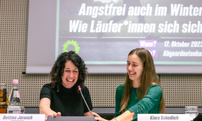 Auf dem Bild sind Bettina Jarasch und Klara Schedlich an einem Tisch mit Mikrophon zu sehen. Beide lachen.