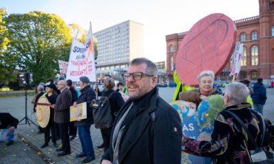 Werner Graf steht in einer Demonstration, er lächelt. Hinter ihm Menschen, die Schilder und Transparente hoch halten