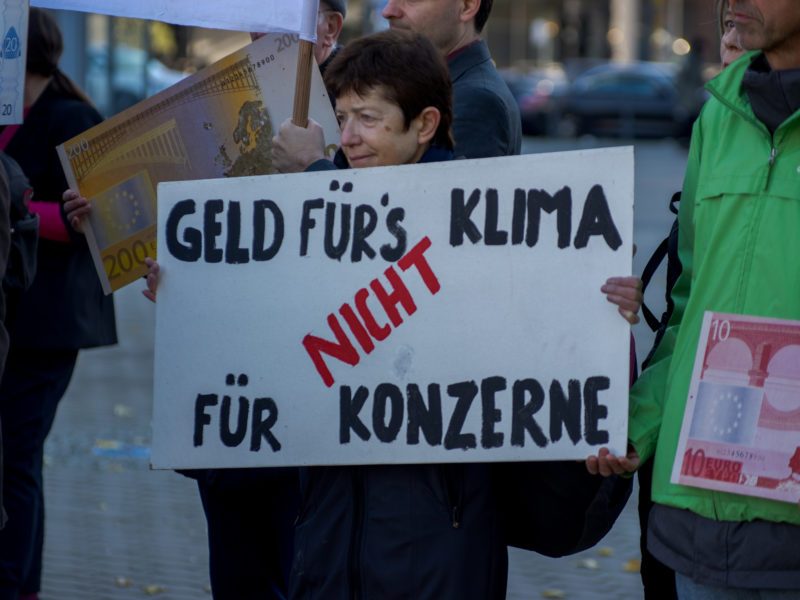 Eine Frau hält ein Demonstrationsschild hoch auf dem steht: "Geld fürs Klima, nicht für Konzerne"