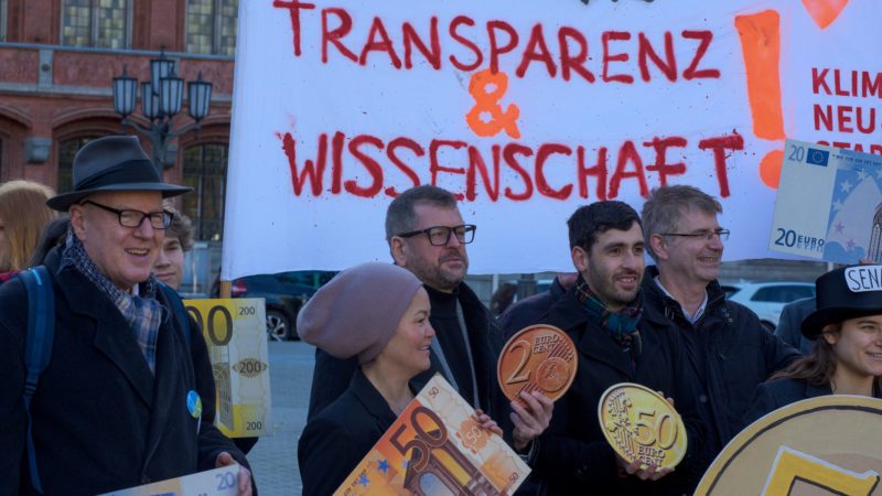 Foto einer Demonstration, mehrere Menschen stehen in einer Gruppe zusammen, unter ihnen Werner Graf. Hinter ihnen ein Transparent.