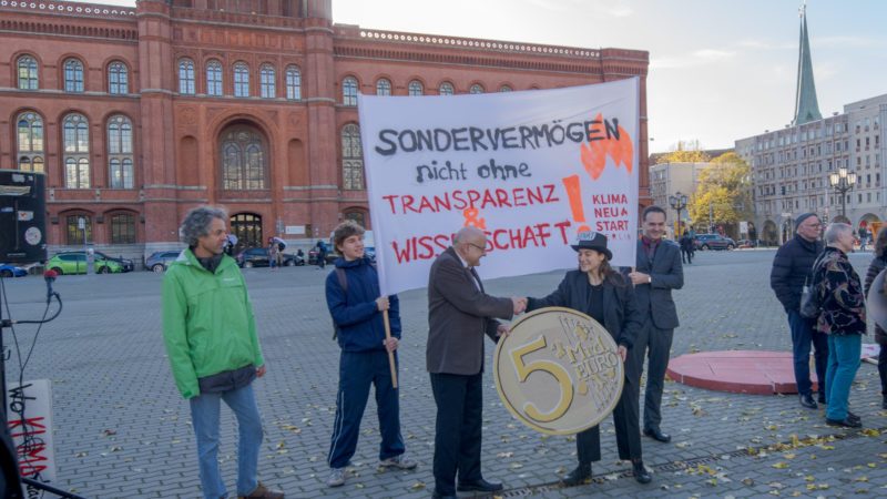 Foto einer Demonstration vor dem Roten Rathaus. Eine kleine Gruppe Menschen hält ein Transparent hoch auf dem steht: "Sondervermögen nicht ohne Transparenz & Wissenschaft"